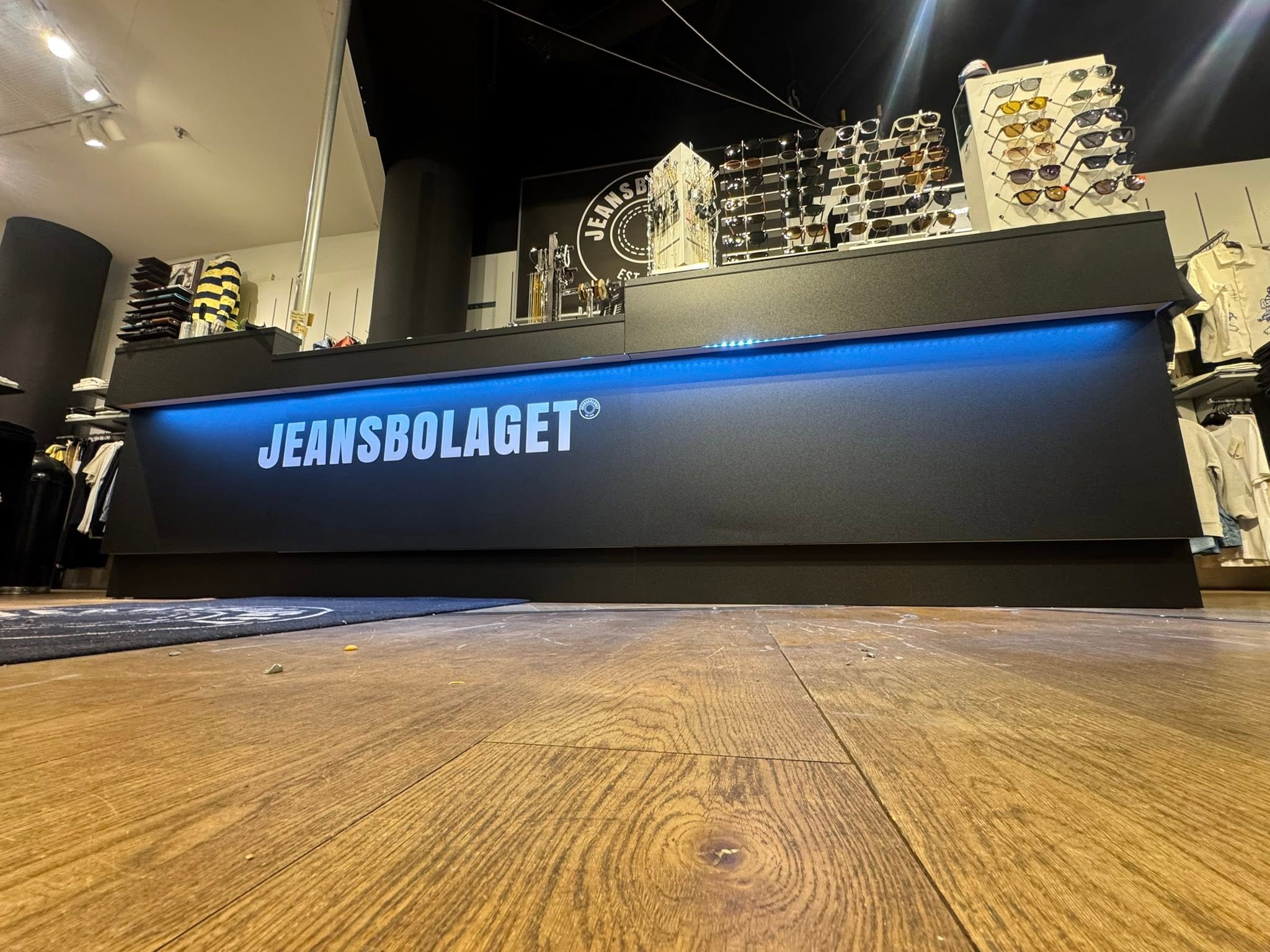 Svart kassa med Jeansbolaget i vitt och blå LED-list mot trägolv