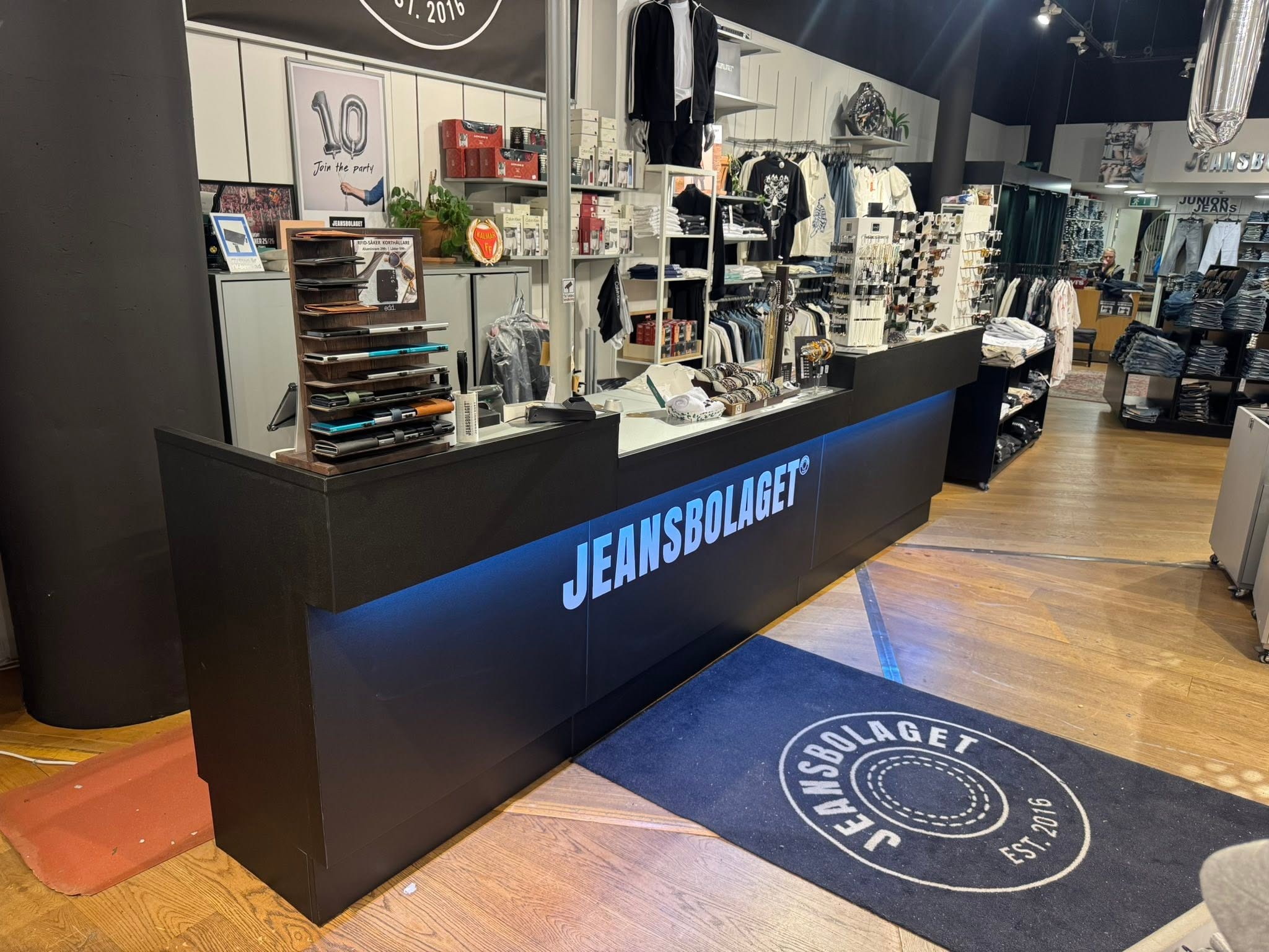 Jeansbolagets butiksinredning med svart disk, trägolv och klädställ